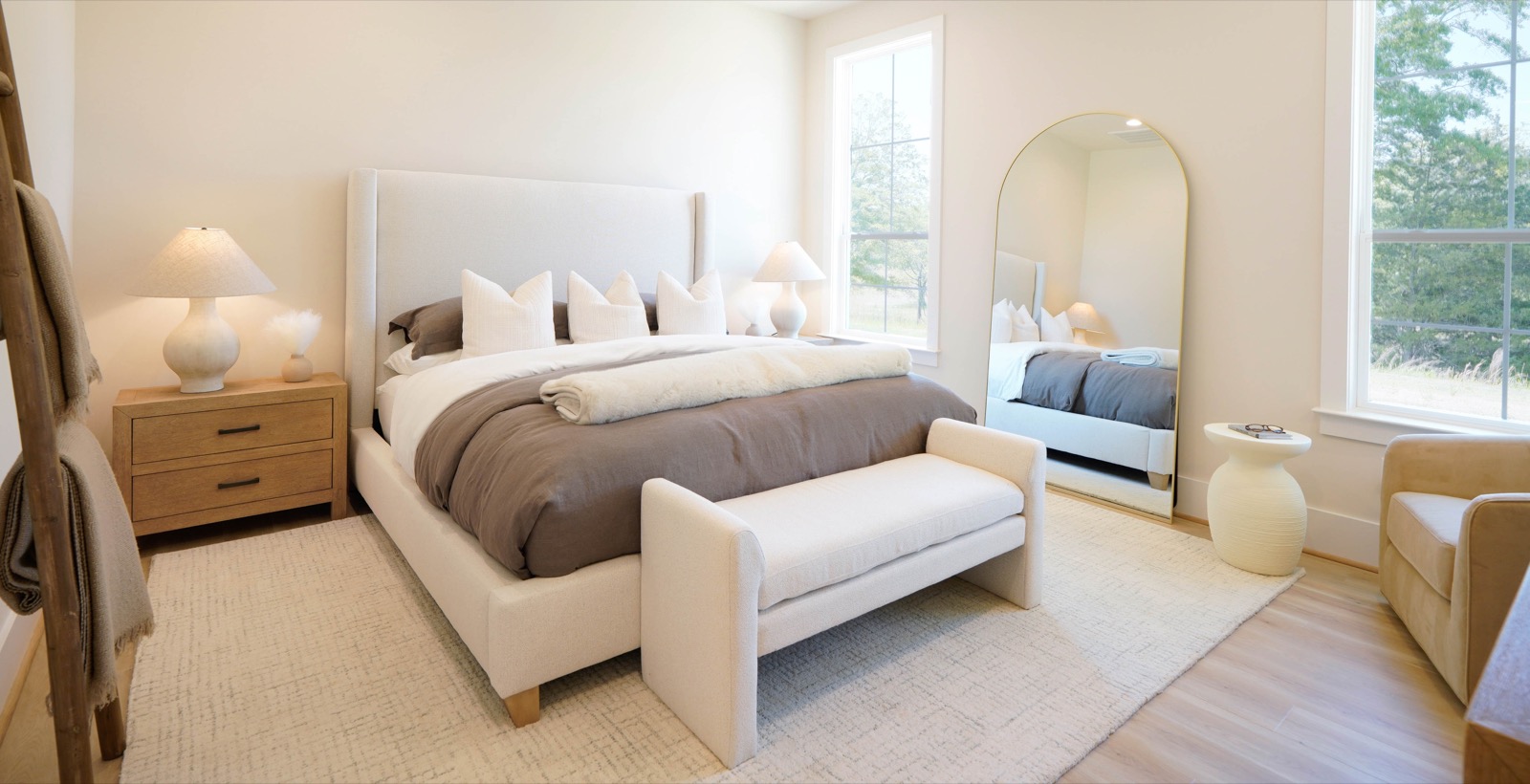 Primary bedroom staged in layered neutrals with an arched mirror